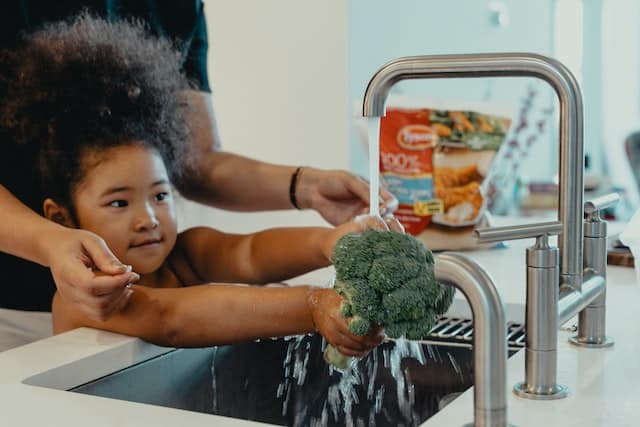 Mother and her daughter washing broccoli on the kitchen sink