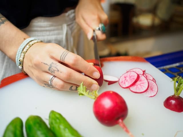 Close-up photo of a woman cutting vegetables as a featured image for a post about ways to design a kitchen for healthy cooking