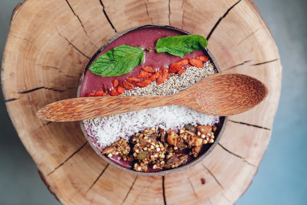 A bowl with a purple smoothie and different toppings with a wooden spoon resting on top of it.